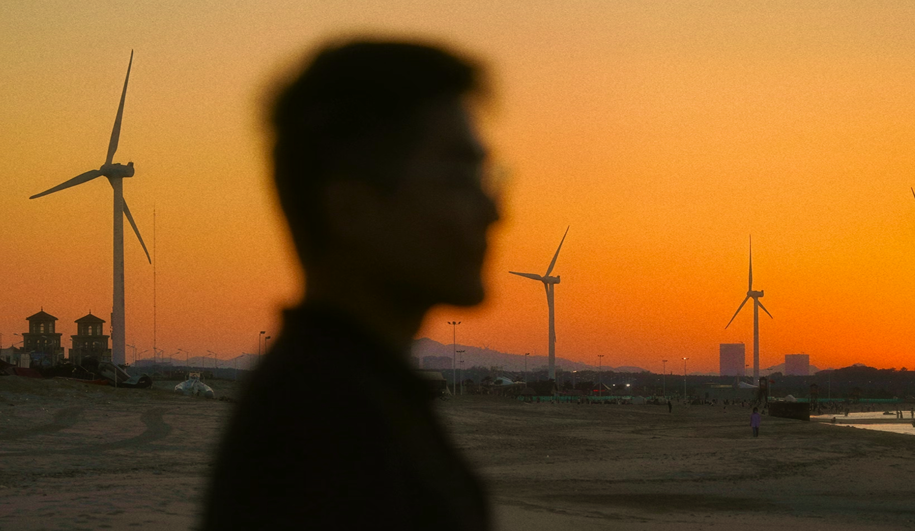 Blurred silhouette of a person with wind turbines in the background at sunset
